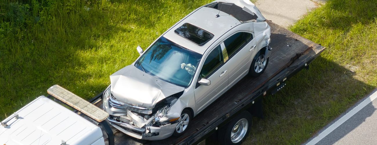Traffic accident with tow truck hauling smashed vehicle on car crash site. First responders helping on road emergency in Florida, USA.